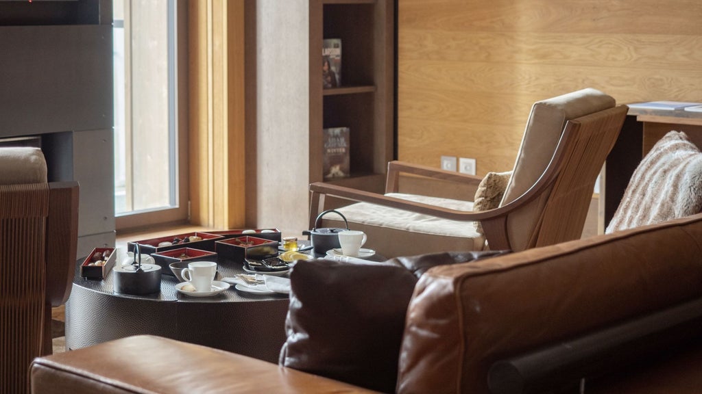 Luxurious alpine suite with modern minimalist design, wooden accents, floor-to-ceiling windows overlooking Swiss mountain landscape at The Chedi Andermatt