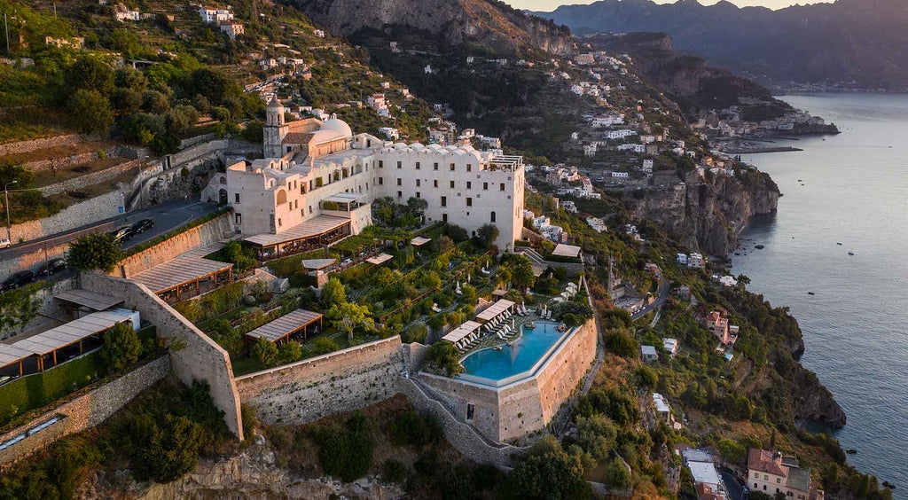 Luxury cliffside hotel overlooking Amalfi Coast, with infinity pool merging into Mediterranean Sea views and terraced gardens