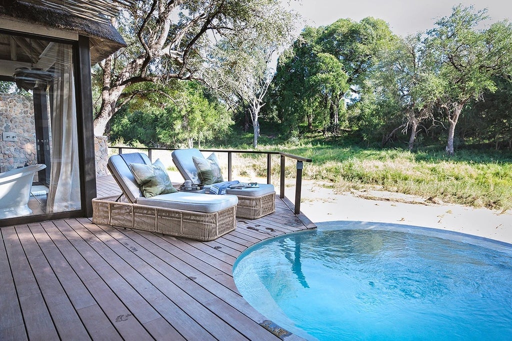 Elegant safari lodge suite with private plunge pool overlooking lush African bushveld, featuring thatched roof and expansive deck