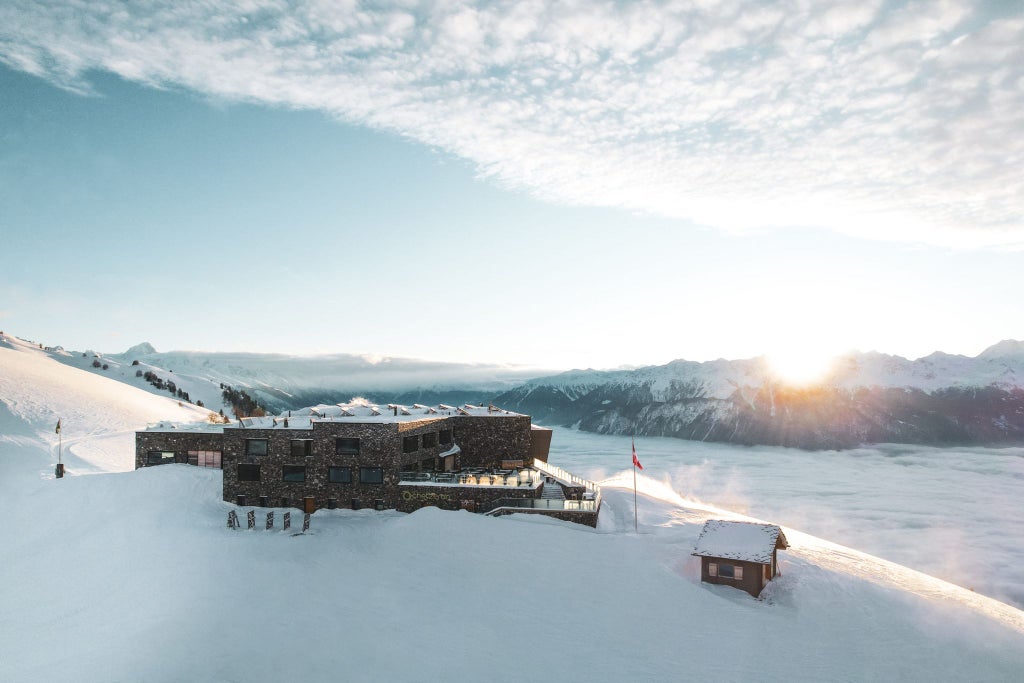 Luxurious mountain hotel Chetzeron perched on alpine slope, panoramic windows revealing stunning Swiss Alps landscape at golden sunset