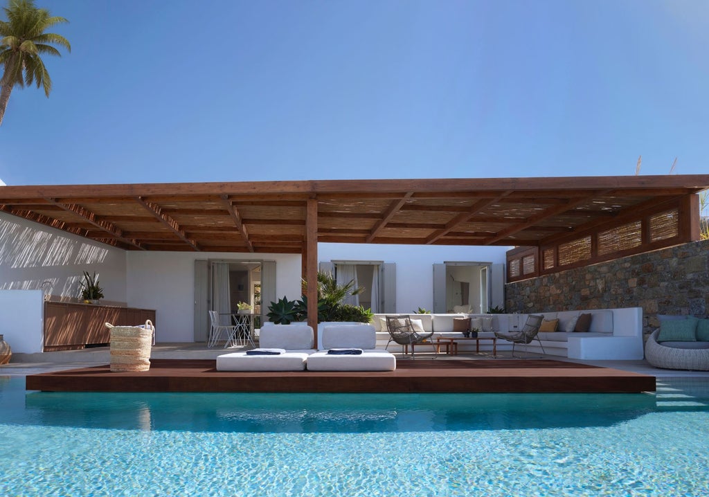 Elegant beachfront villa with infinity pool overlooking Aegean Sea at sunset, featuring white minimalist architecture and luxury loungers