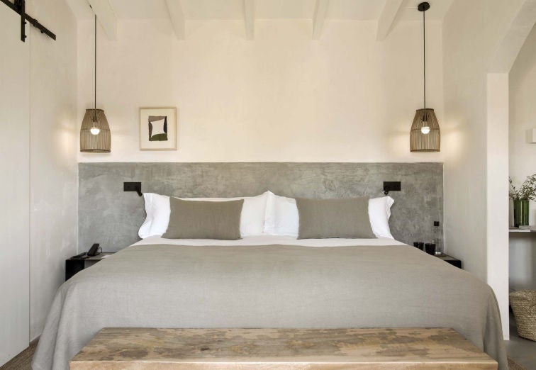 Elegant junior suite with rustic stone walls, king bed with crisp white linens, terrace views of Spanish countryside, and natural decor