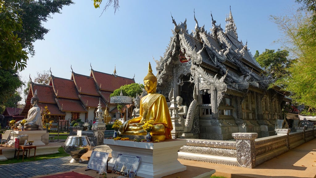 Buddhist temple pavilion with ornate golden decor and red roof nestled among lush greenery at sunset in Chiang Mai's mountains