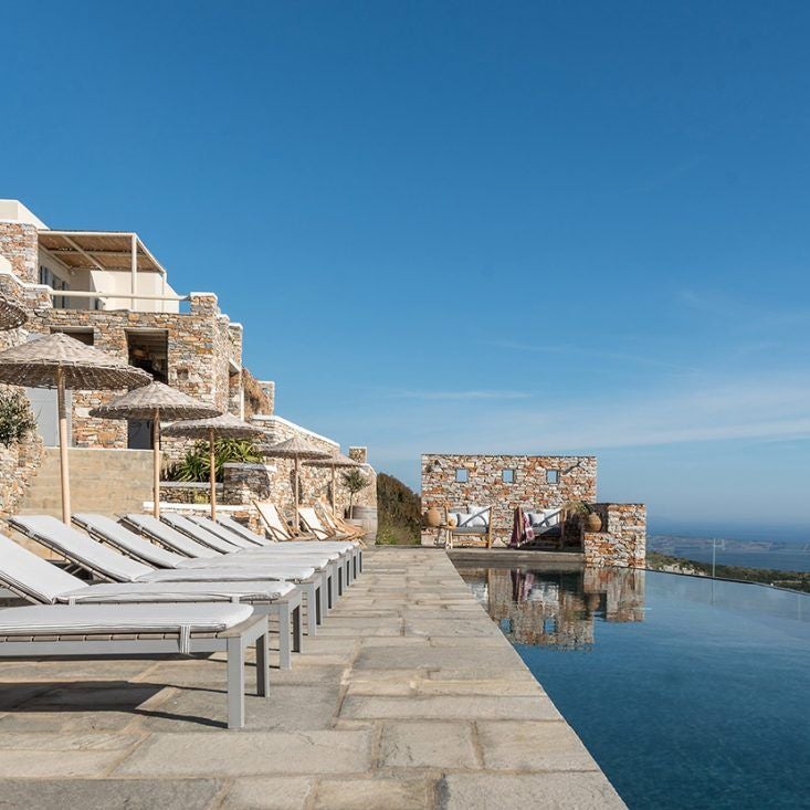 Luxurious white-washed Cycladic hotel overlooking the azure Aegean Sea, with minimalist design and infinity pool against Sifnos island's dramatic landscape