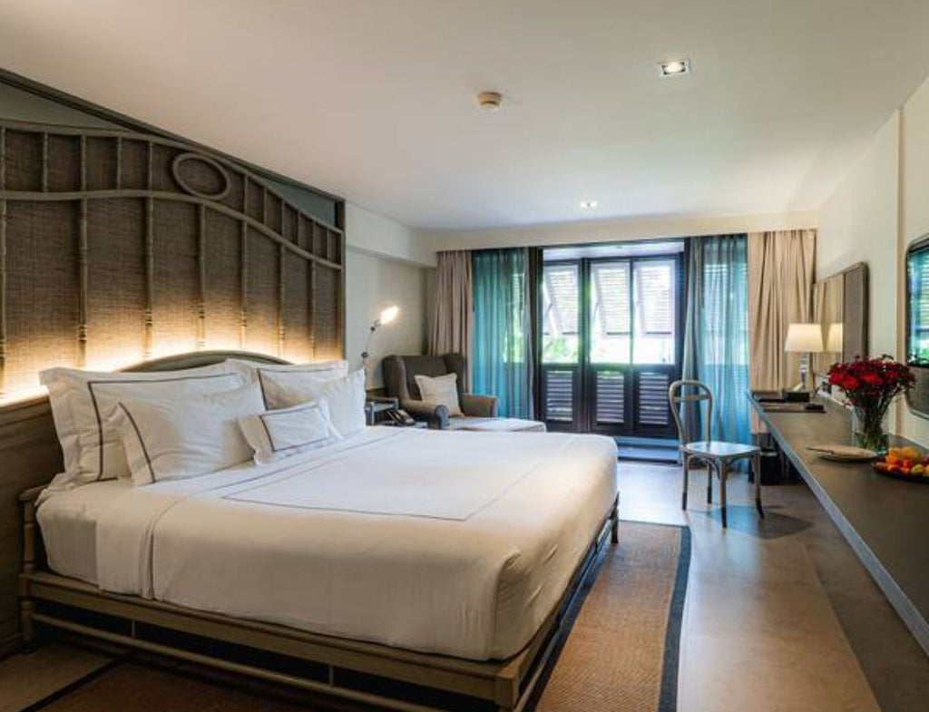 Modern luxury hotel room with king bed, floor-to-ceiling windows, dark wood furnishings, crisp white linens, and contemporary Thai decor