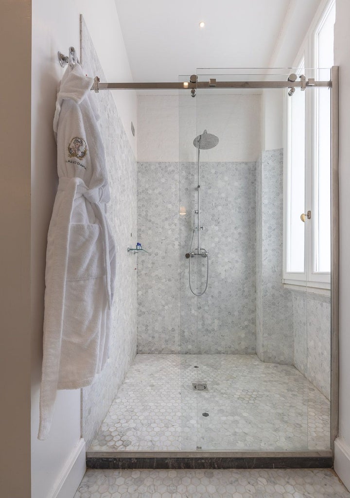 Elegant garden suite with plush white bedding, marble floors, and French doors opening to a lush Italian courtyard in Rome's Palazzo Dama hotel