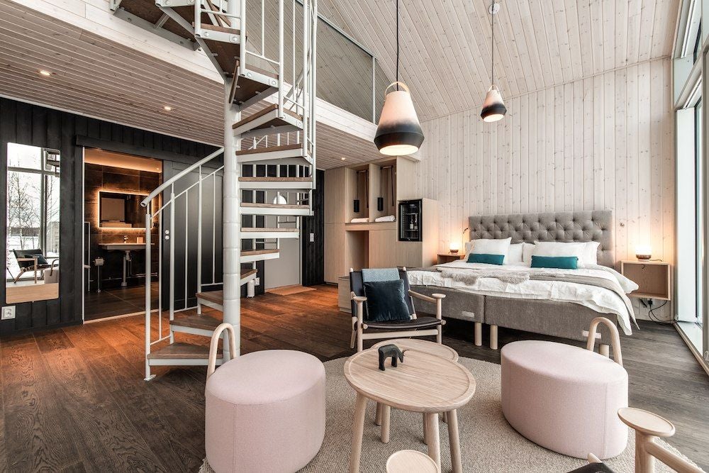 Minimalist wooden interior of Arctic Bath Land Cabin Family room, featuring rustic Scandinavian design with warm timber tones and large window overlooking snowy landscape
