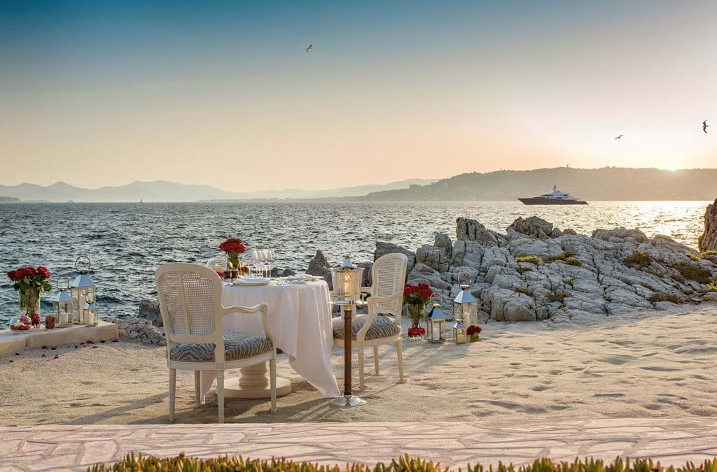 Historic luxury hotel in Cap d'Antibes with white facade and palm trees overlooking Mediterranean Sea from clifftop location