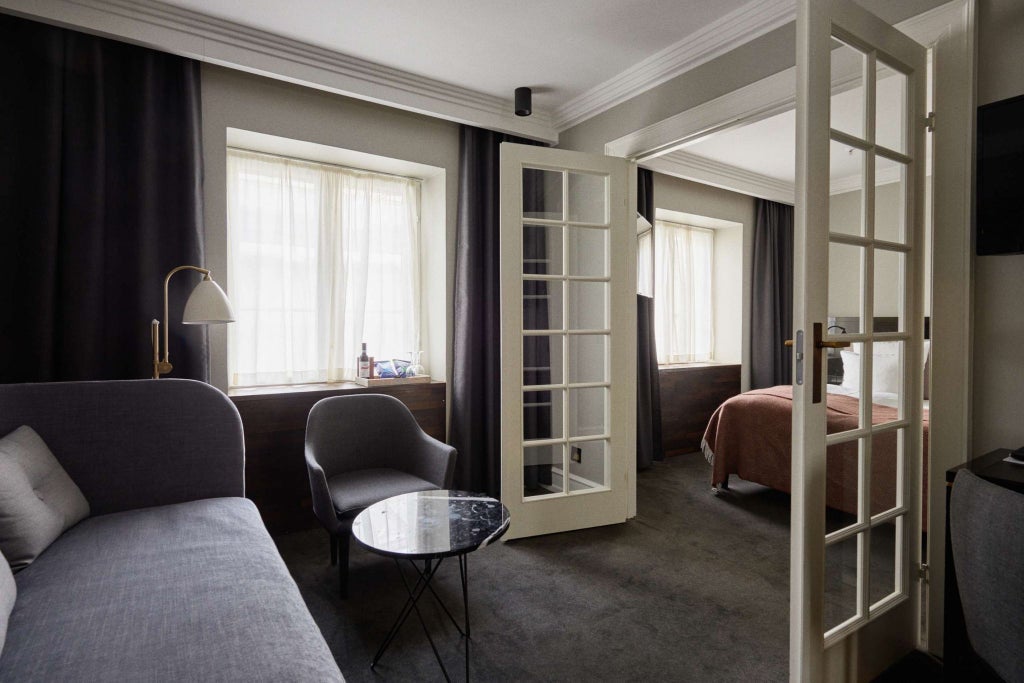 Elegant Danish junior suite with modern minimalist design, soft neutral color palette, premium furnishings, and large window overlooking urban landscape