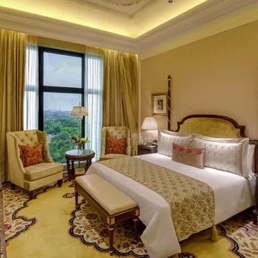 Opulent Maharaja Suite at scenset Palace with regal gold and cream decor, ornate chandelier, plush king bed, and panoramic city view through large windows