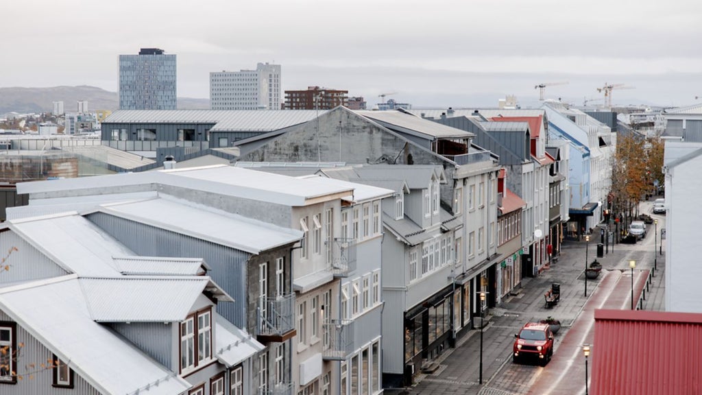 Sleek, modern ION City Hotel exterior with minimalist Nordic design, glass facade reflecting Reykjavik's dramatic urban landscape and mountainous horizon at twilight.