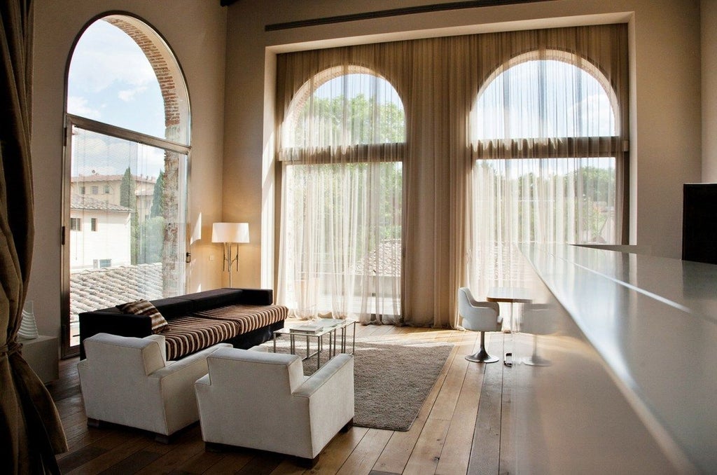 Minimalist Italian loft suite with exposed wooden beams, neutral palette, modern furniture, and large windows overlooking scenic landscape in Florence