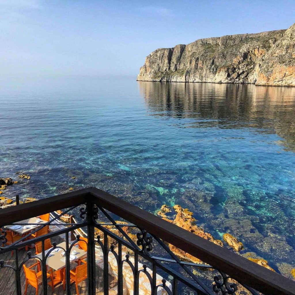 Luxurious stone-built seaside hotel with traditional Mani architecture, nestled against azure Aegean waters and rocky coastline at sunset