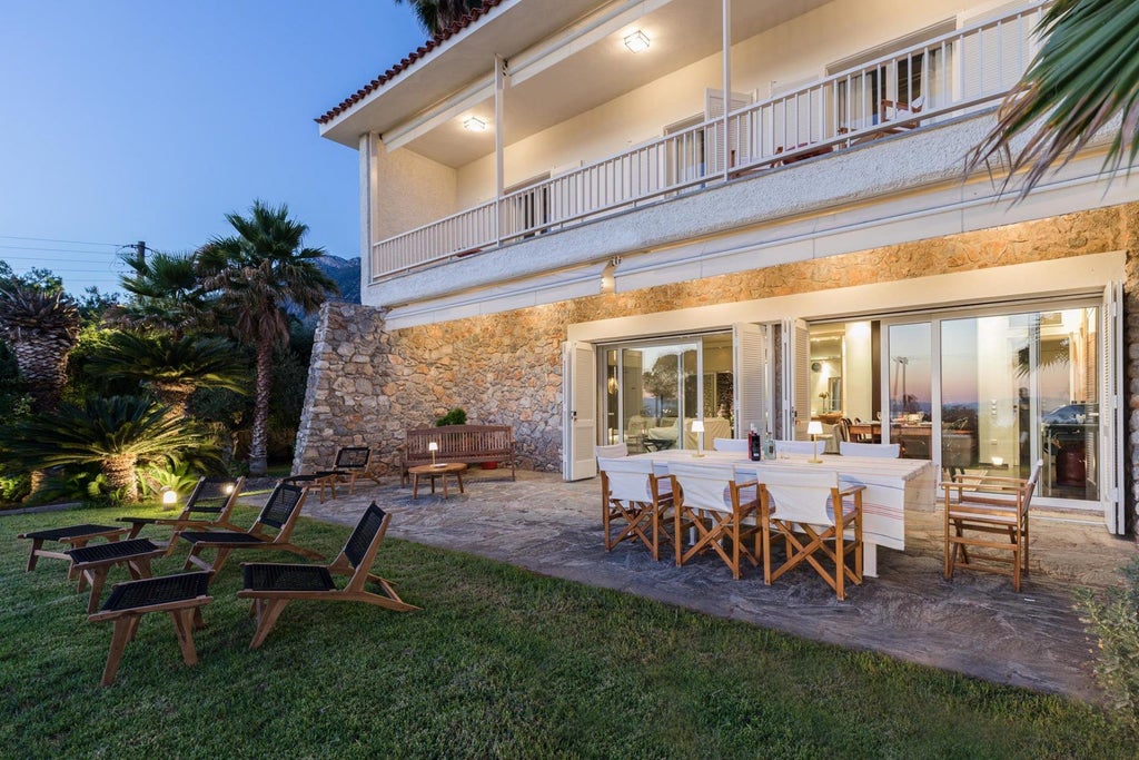 Elegant stone villa with blue shutters nestled in a lush Greek landscape, showcasing traditional Mani architecture with panoramic Aegean Sea views