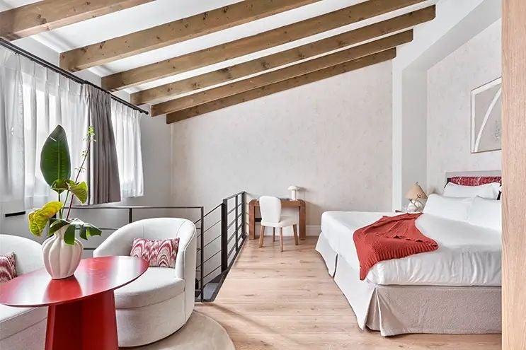 Elegant duplex hotel room at Posada Terra Santa, featuring rustic wooden floors, white linens, classic Spanish architectural details, and warm natural lighting