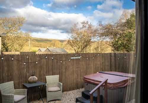 Elegant boutique hotel room with plush white bedding, exposed stone walls, modern furnishings, and large windows overlooking scenic countryside landscape