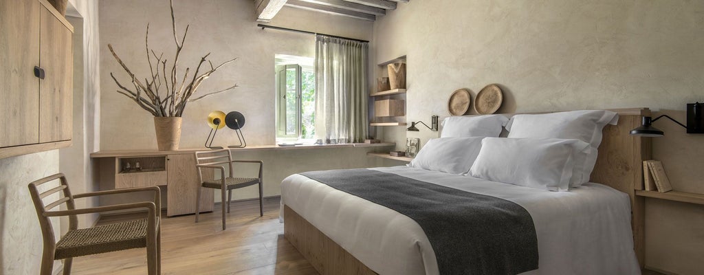 Elegant superior room at Badia di Pomaio, showcasing rustic Tuscan design with wooden floors, plush white bedding, and minimalist decor highlighting Italian countryside charm