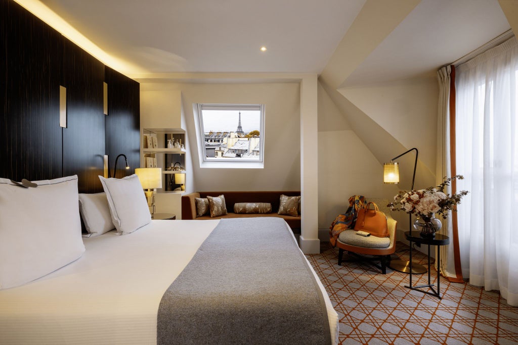 Luxurious Parisian suite with elegant cream and grey decor, plush king bed, marble bathroom, and floor-to-ceiling windows overlooking chic city streetscape