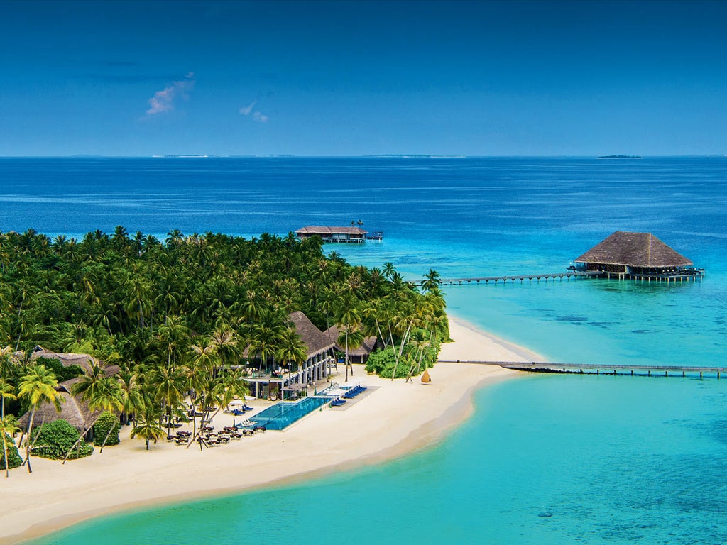 Luxurious overwater villas with thatched roofs and private pools stretch along wooden walkways over crystal-clear turquoise Maldivian lagoon