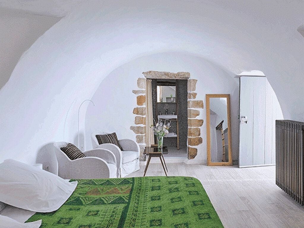 Elegant stone-walled bedroom with luxurious white linens, rustic wooden furniture, and soft natural light in a French countryside hotel