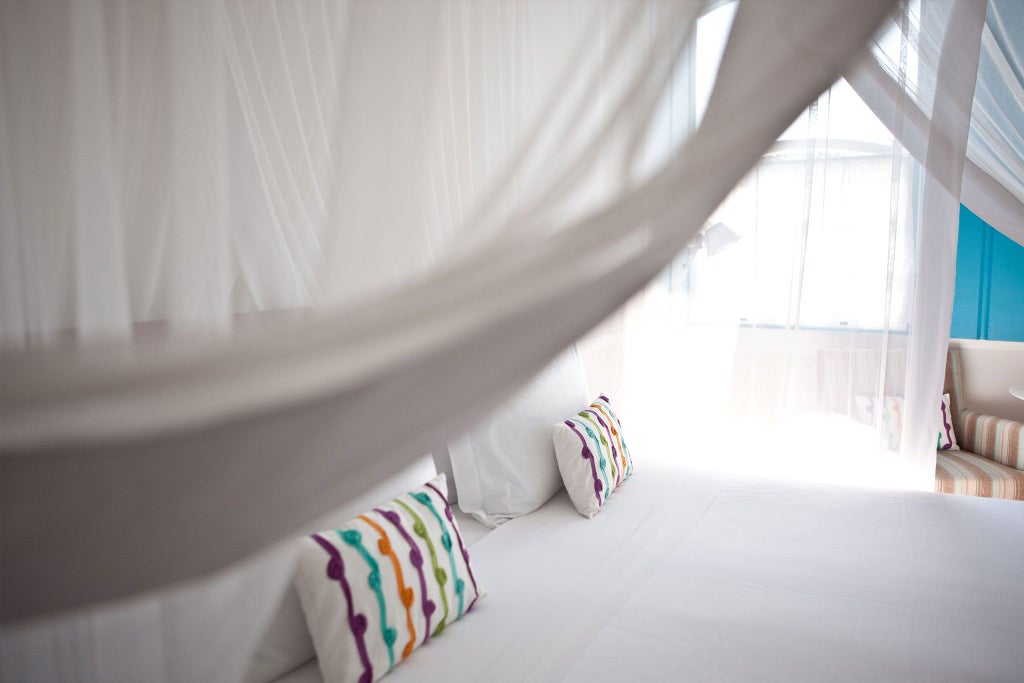 Elegant turquoise-themed luxury suite with plush white bedding, ornate wooden furniture, and large windows overlooking tropical Brazilian scenery