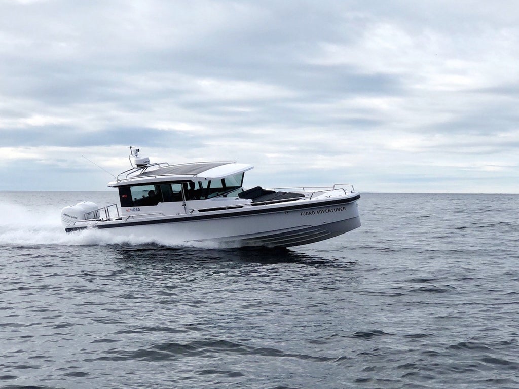 Scenic Norwegian fjord with sleek boat navigating crystal-clear waters, surrounded by dramatic snow-capped mountains and lush green landscapes under soft Nordic light