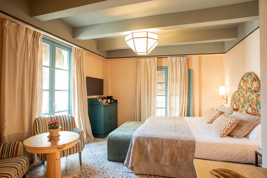 Elegant whitewashed Spanish colonial room with wooden furniture, arched windows, and pristine white linens in Seville's historic Hospes hotel