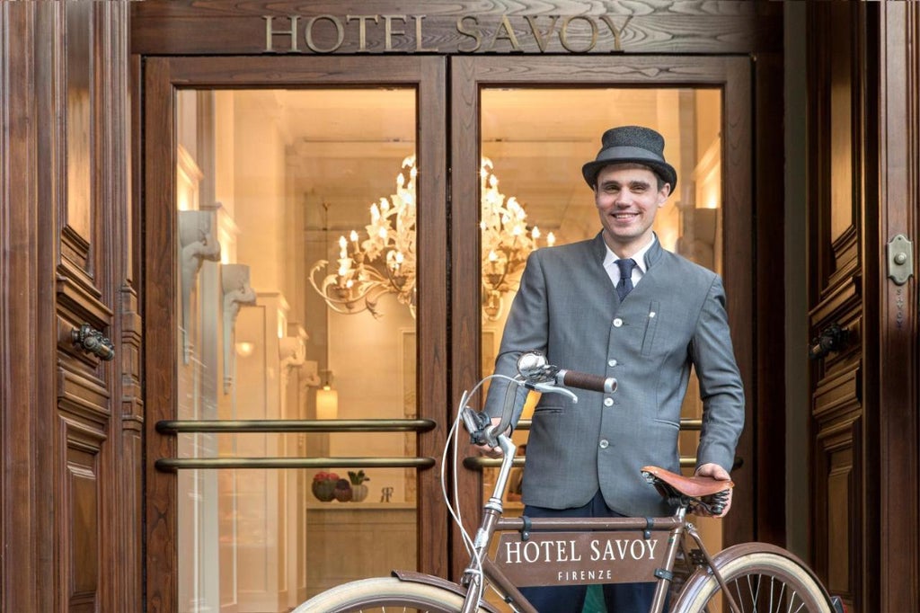 Grand Hotel Savoy's elegant beige Renaissance facade with ornate balconies, towering arched windows, and manicured hedges in Florence, Italy