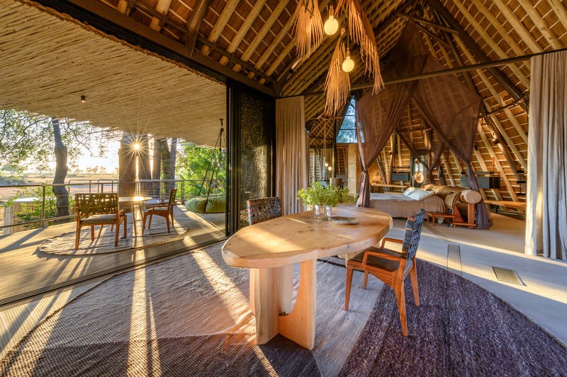 Elevated luxury safari lodge with thatched-roof villas perched on wooden stilts above wetlands at sunset in the Okavango Delta