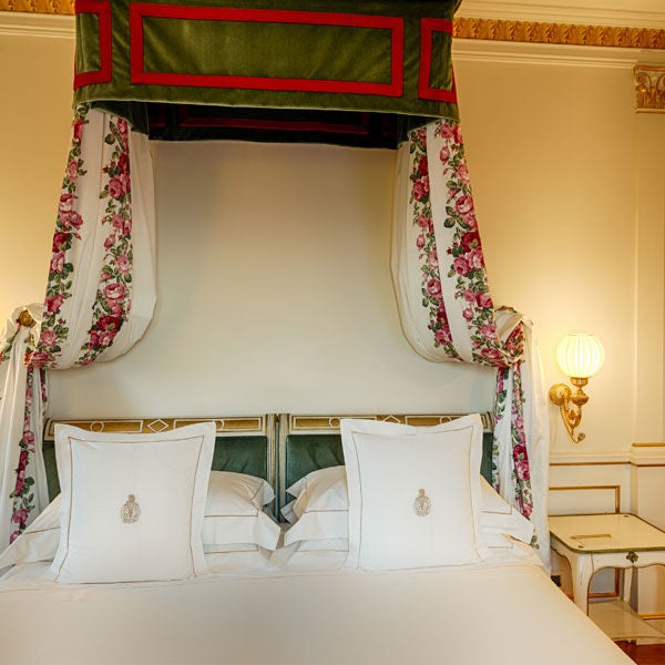 Elegant Classic hotel room with ornate gold-framed artwork, antique furnishings, crystal chandelier and plush king bed with red accents