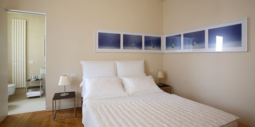 Elegant Italian villa bedroom with private pool view, soft rosemary-toned linens, wooden furnishings, and panoramic Tuscan landscape beyond large windows