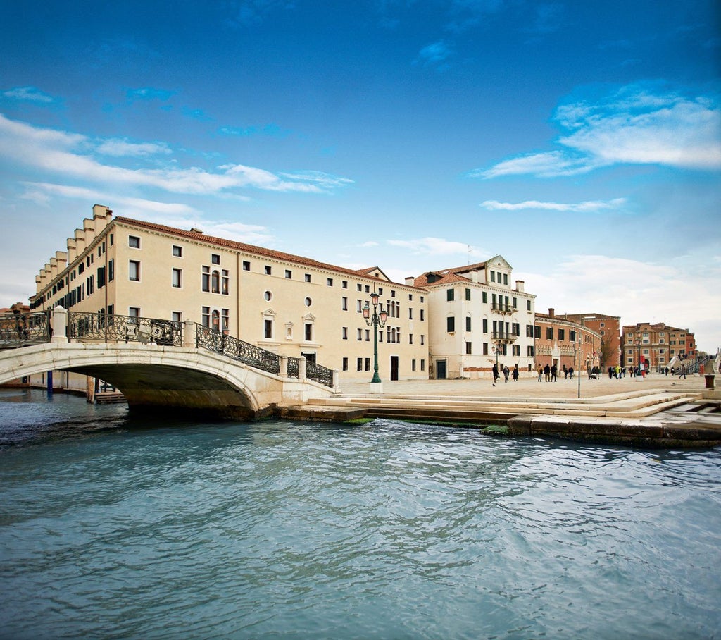 Elegant waterfront luxury hotel in Venice with ornate stone architecture, arched windows, and private dock overlooking the lagoon at sunset