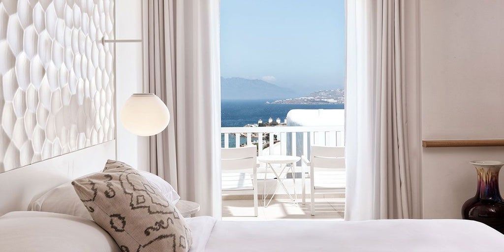 Luxurious white-washed Ocean suite with panoramic Aegean Sea view, minimal Cycladic design, private balcony, and infinity pool overlooking scenset landscape