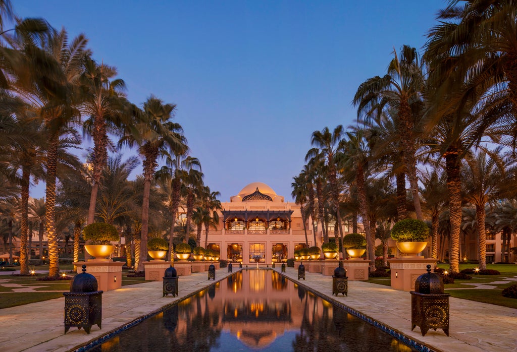 Ornate Arabian-style luxury hotel with grand archways, palm trees and turquoise pools reflecting in calm waters at sunset in Dubai