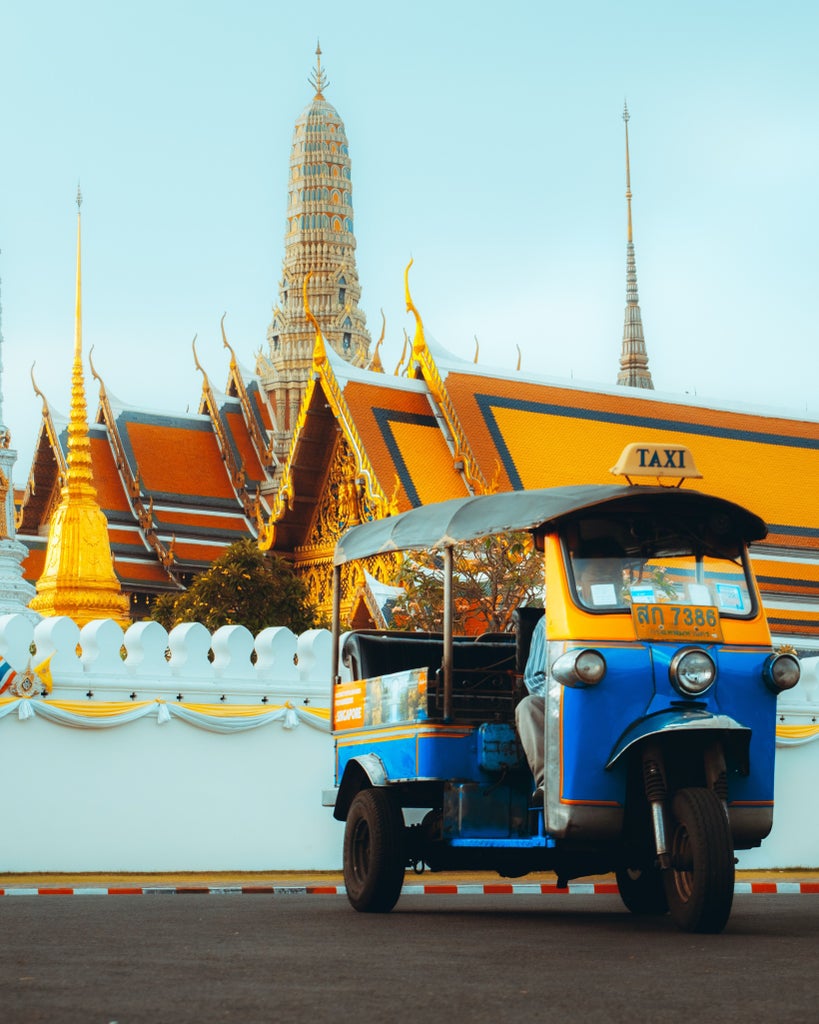 Opulent golden temple spires gleam against Bangkok's skyline, showcasing intricate Thai architectural details and vibrant royal blue skies at midday