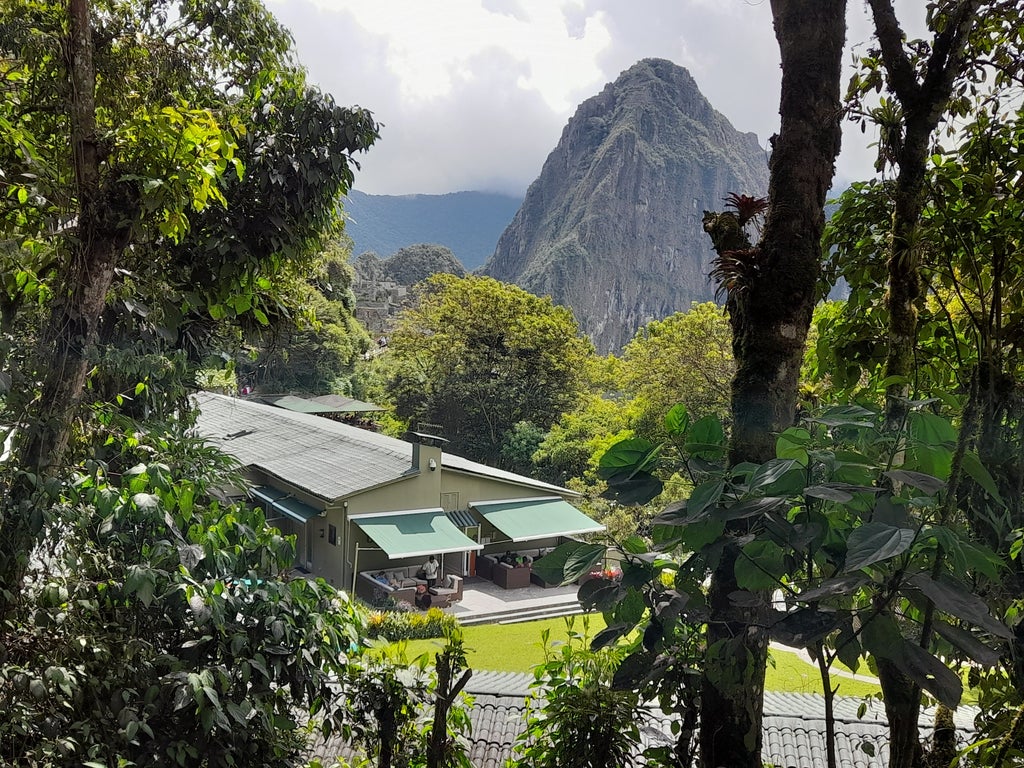 Modern luxury mountain lodge with stone walls and thatched roof nestled at the foot of Machu Picchu, surrounded by lush Andean peaks