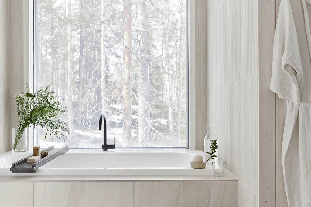 Modern wooden cabin-style suite with large panoramic windows overlooking snowy Finnish forest, featuring minimalist Nordic design and cozy interior lighting at dusk