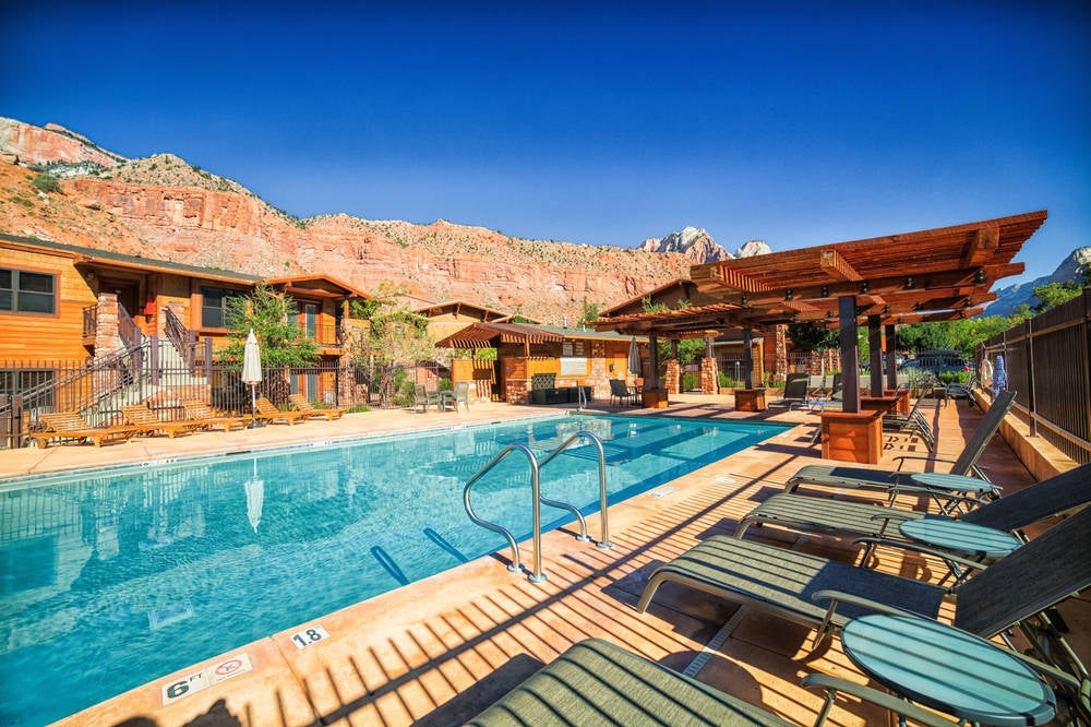 Modern rustic lodge exterior with stone facade nestled against red rock cliffs, featuring expansive windows and timber accents