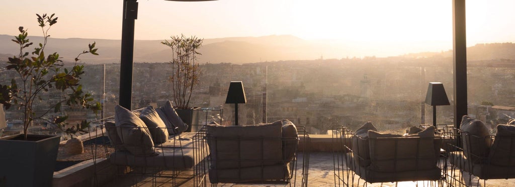 Luxurious Moroccan riad courtyard with intricate zellige tiles, ornate archways, and traditional fountain against soft evening light in Fès