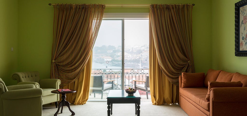 Elegant hotel room with balcony overlooking Porto's Douro River, featuring modern decor, king bed, and panoramic floor-to-ceiling windows