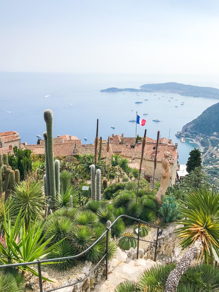 Panoramic view of luxury yachts moored in azure waters of Nice harbor at sunset, with pastel-colored buildings along the promenade