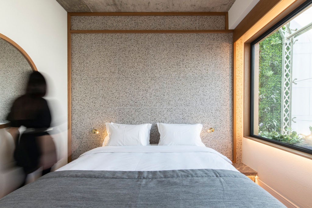 Minimalist hotel room with wooden floors, crisp white linens, and warm ambient lighting, showcasing modern Greek design in a compact urban space.