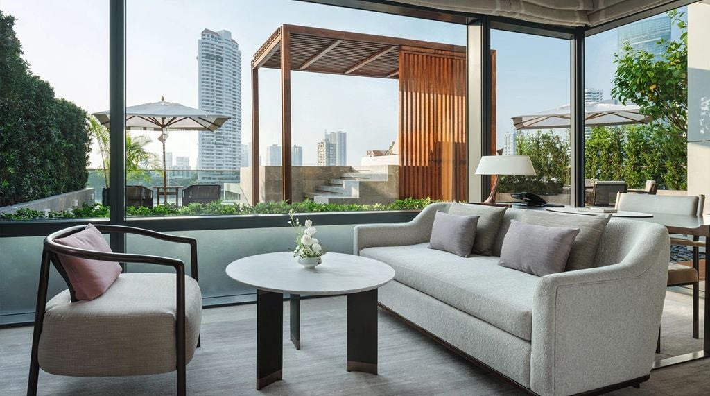 Elegant riverside suite at Capella Bangkok featuring floor-to-ceiling windows, plush king bed, and private terrace with Chao Phraya views