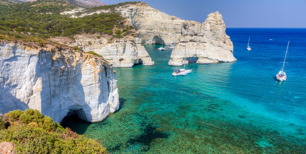 Ancient whitewashed houses cascade down rocky cliffs overlooking the turquoise Aegean Sea, with traditional Greek architecture and blue domes