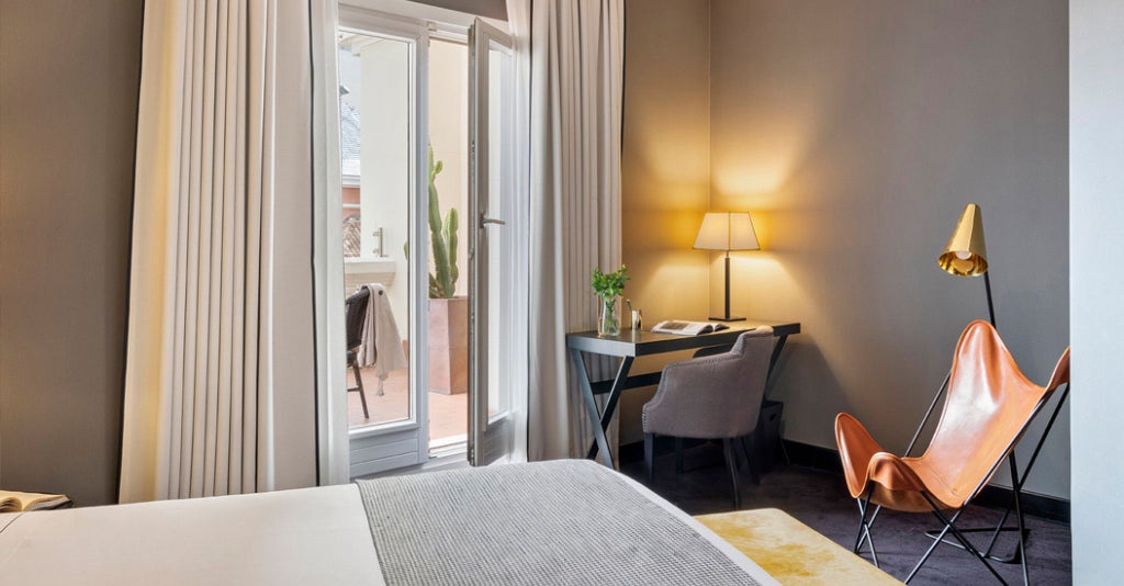 Luxurious deluxe terrace room at The Principal Madrid, featuring elegant modern decor, plush furnishings, and a sweeping view of city architecture through large windows