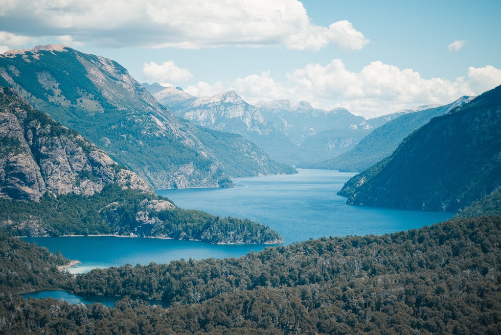 Scenic view of snow-capped Andes mountains surrounding pristine Lake Nahuel Huapi in Bariloche, framed by lush evergreen forest