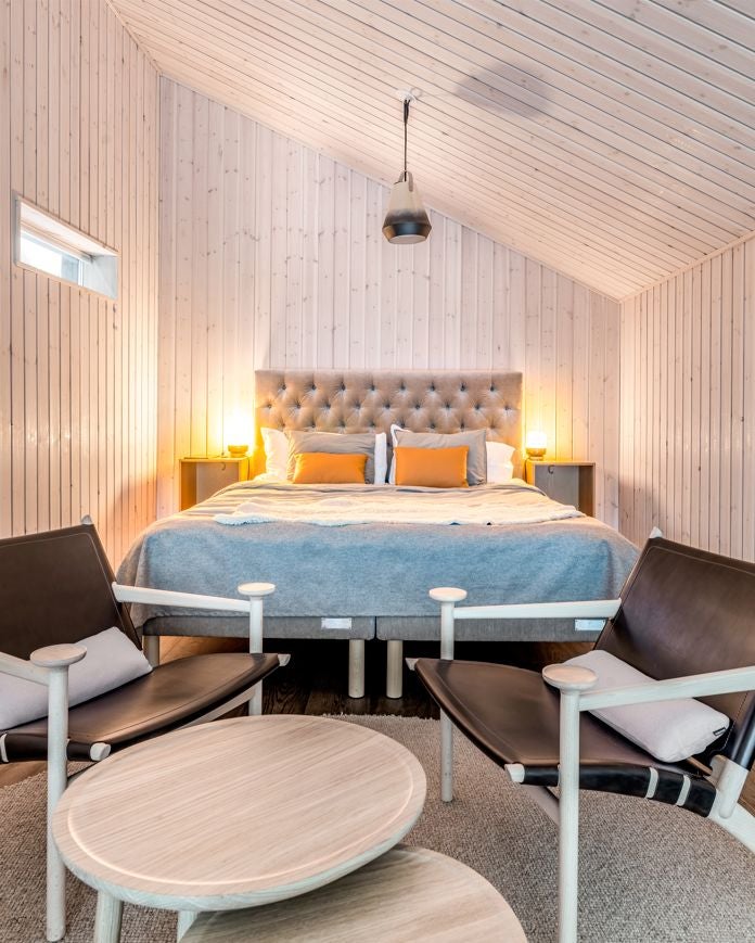 Minimalist Nordic wooden suite with floor-to-ceiling windows, modern rustic design, warm lighting, overlooking snow-covered pine forest landscape in Arctic region