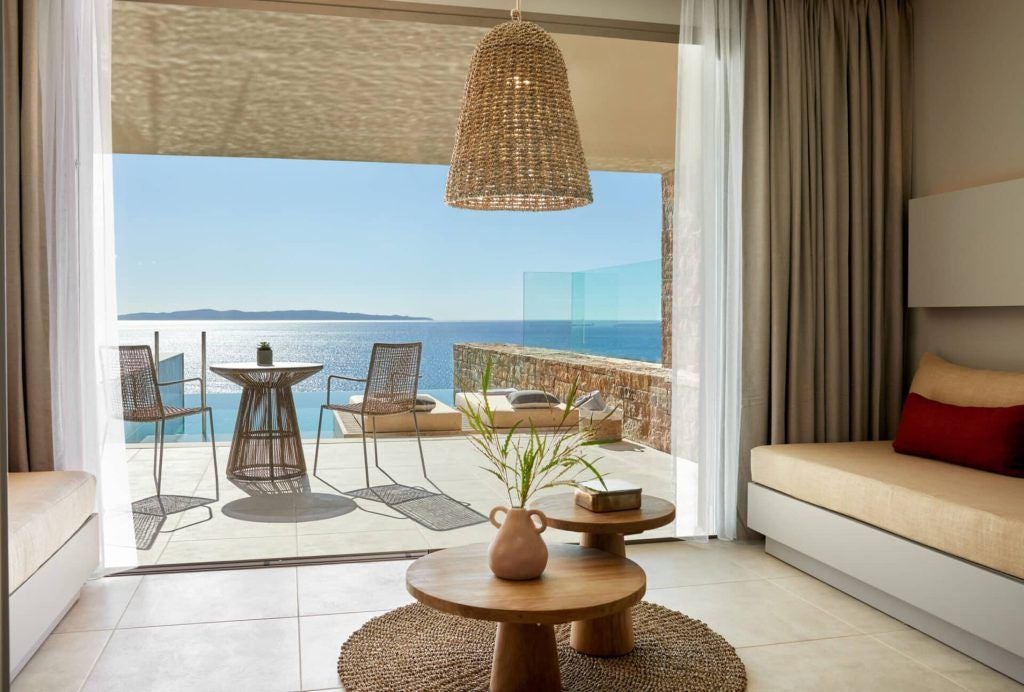 Spacious family suite with direct pool access, elegant modern decor, and panoramic views of the Mediterranean coastline in scenic coastal Greece.