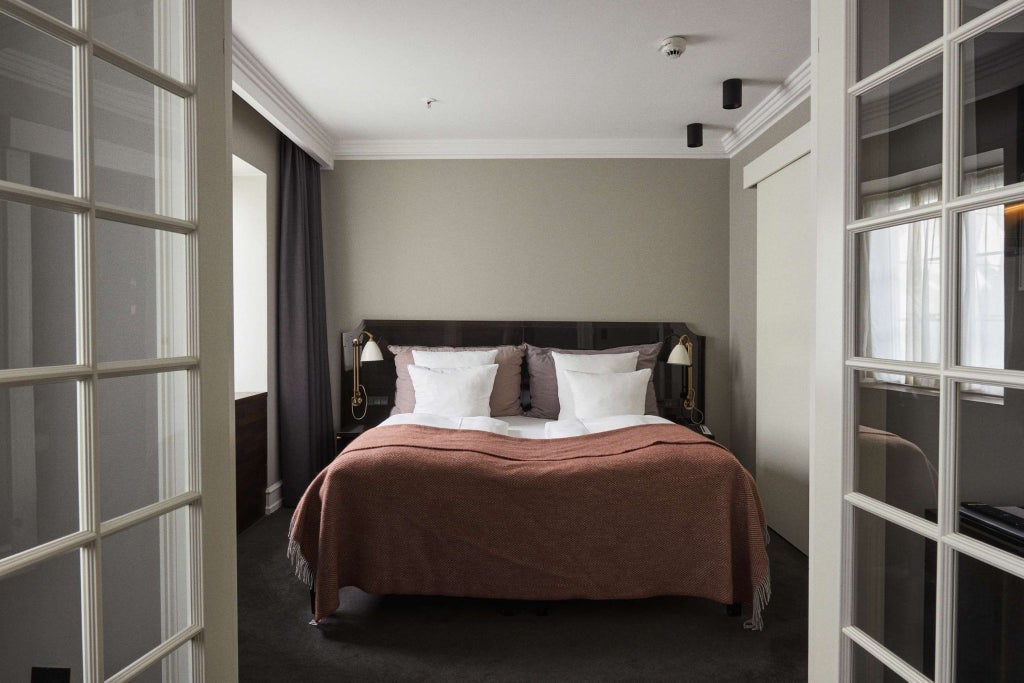 Elegant Danish junior suite with soft neutral tones, plush white bedding, modern minimalist design, and large window with natural light streaming in