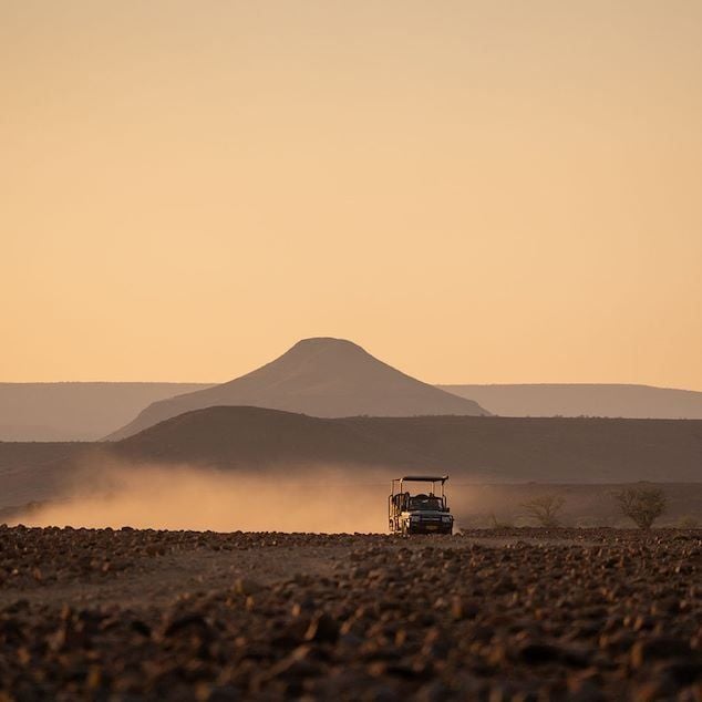 Luxurious desert lodge nestled in Namibian landscape, featuring rustic stone bungalows with panoramic views of sweeping sand dunes and rugged terrain at sunset